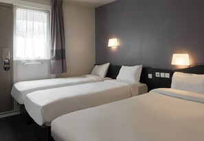 Habitación de hotel con dos camas individuales, una puerta con cerradura, una ventana con cortinas y dos lámparas fijadas a la pared.