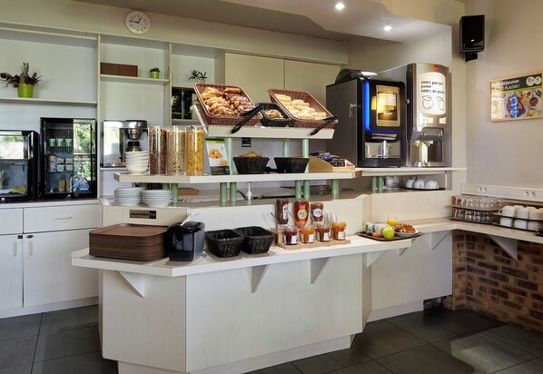 Ein Frühstücksbuffet mit verschiedenen Speisen, einer Kaffeemaschine und einer Uhr an der Wand.