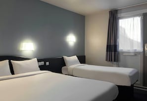 A hotel room with two beds, a headboard, a window with curtains, and wall-mounted lights. - B&B Hotel Saclay (Gif-sur-Yvette)