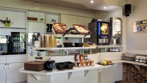 En morgenmadsbuffet med forskellige spisemuligheder, en kaffemaskine og et ur på væggen.