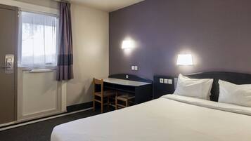 A hotel room with a bed, a desk, a chair, a window with curtains, and two wall-mounted lights.