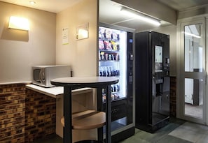 A compact kitchenette with a microwave, a small table, and a beverage vending machine.