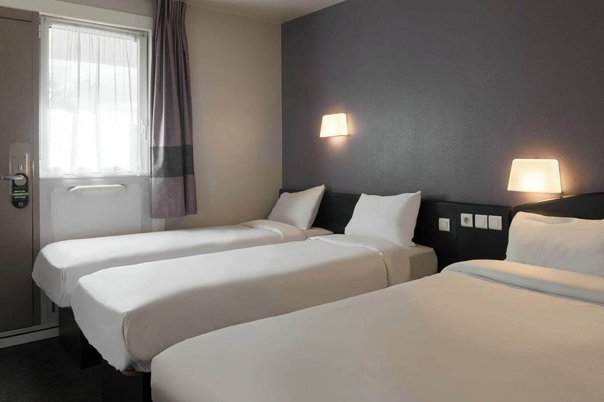 Habitación de hotel con dos camas individuales, una puerta con cerradura, una ventana con cortinas y dos lámparas fijadas a la pared.