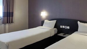 Habitació d'hotel amb dos llits individuals, una tauleta de nit, una làmpada i una finestra amb cortines.