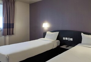 Habitación de hotel con dos camas individuales, una mesita de noche, una lámpara y una ventana con cortinas.