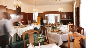 Comedor formal con varias mesas dispuestas para una comida, sillas de madera y candelabros.