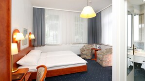 Una habitación de hotel con cama, escritorio, silla, lámpara, espejo y ventana con cortinas.