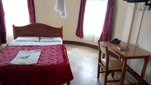 A hotel room with a bed, a desk, a chair, a TV, and a window with curtains. - Nanyuki Simba Lodge (Nanyuki)