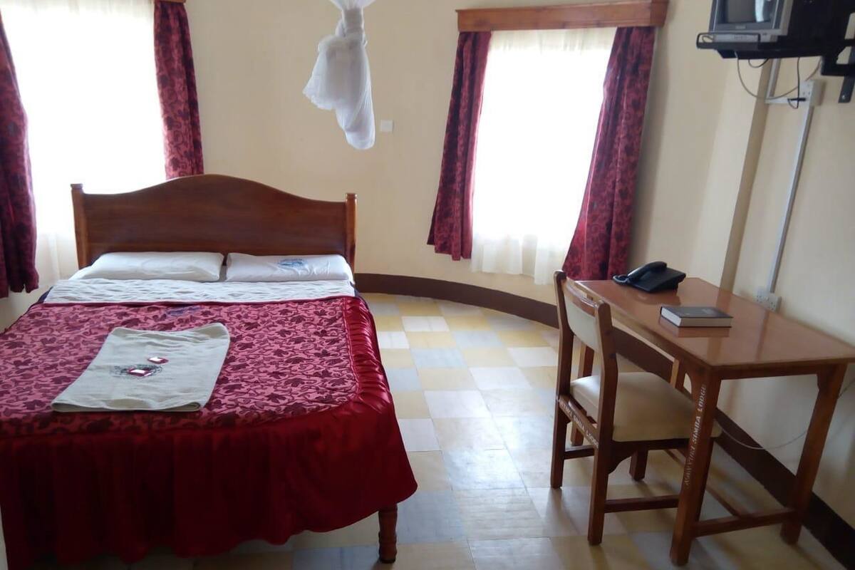 A hotel room with a bed, a desk, a chair, a TV, and a window with curtains.