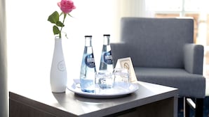 A table with a vase of a pink rose, two water bottles, and a glass on a tray.