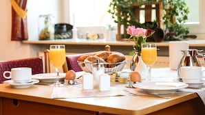 A breakfast table with a bowl of bread, a vase of flowers, and a pitcher of orange juice.