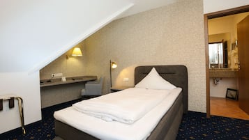 A hotel room with a neatly made bed, a desk with a chair, a small table, and a mirror.