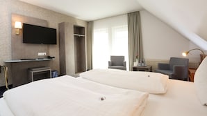 A hotel room with two beds, a flat-screen TV mounted on the wall, a desk with a lamp, and a chair.