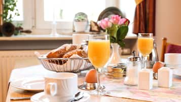 Una mesa de desayuno con cruasanes, zumo de naranja y un florero con flores.