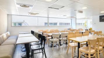 Un comedor moderno con varias mesas y sillas, un sofá, y un amplio ventanal con vistas a edificios.