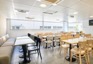 Un espace repas moderne, doté de plusieurs tables et chaises, d’un canapé et d’une grande fenêtre offrant une vue sur les bâtiments.