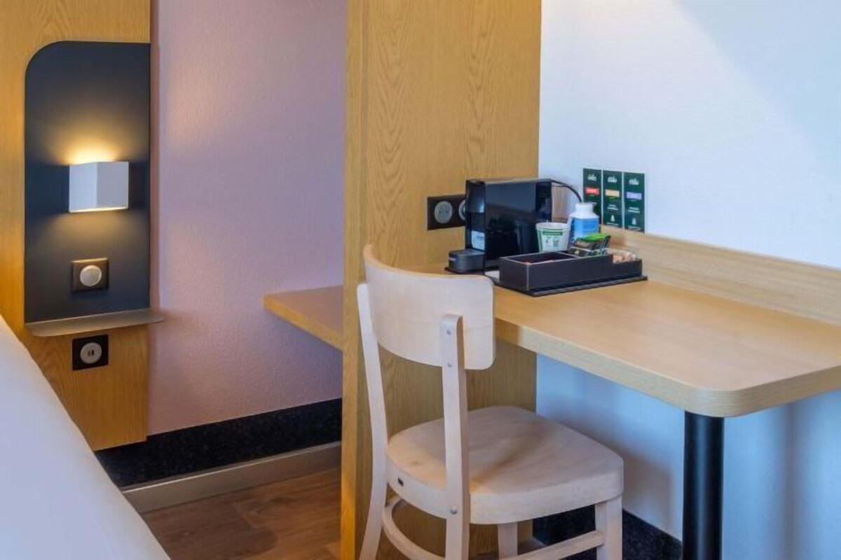 Een hotelkamer met een houten bureau, een witte stoel, een koffieapparaat en een wandlamp.