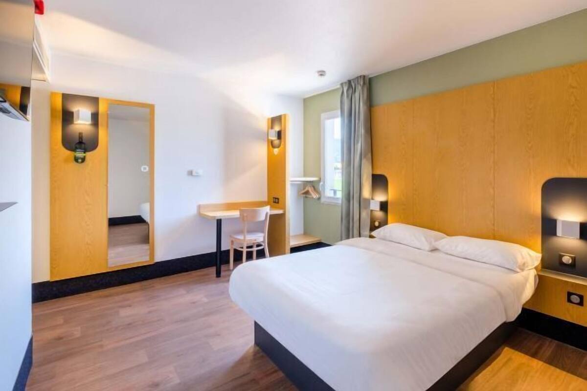 Une chambre d’hôtel avec un lit, un bureau, une chaise et un miroir.