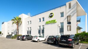 A modern hotel with a white facade, a prominent 'HOTEL' sign, and a parking lot with several cars. - B&B Hotel Cannes La Bocca Plage (Cannes)