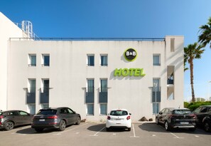 Un edifici d'hotel modern amb un rètol que diu "B&B HOTEL" i diverses places d'aparcament al davant.