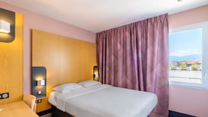 A hotel room with a bed, a desk, and a window with curtains. - B&B Hotel Cannes La Bocca Plage (Cannes)
