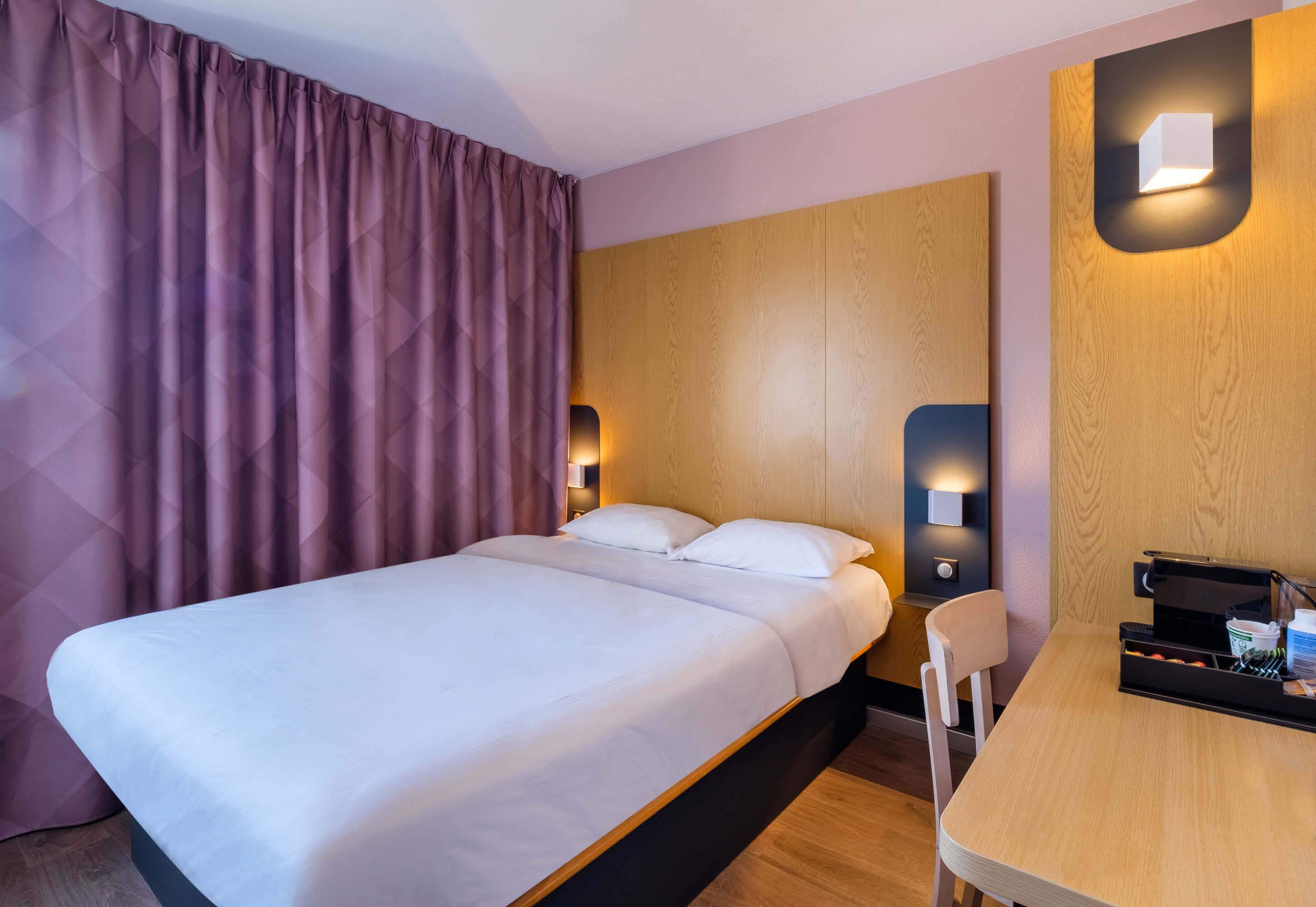 A neatly made bed with white linens, a wooden headboard, and two bedside lamps.