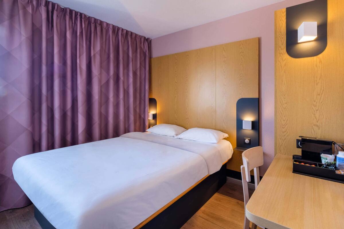 Un lit bien fait, avec du linge de lit blanc, une tête de lit en bois et deux lampes de chevet.