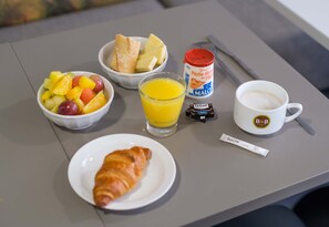 A breakfast table with croissant, fruit salad, bread, juice, coffee, and a travel-sized coffee maker. - B&B Hotel Cannes La Bocca Plage (Cannes)