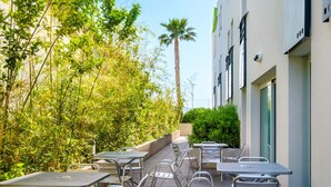 Eine Außenpatio mit Metalltischen und -stühlen, umgeben von üppiger Bepflanzung und einer hohen Palme.