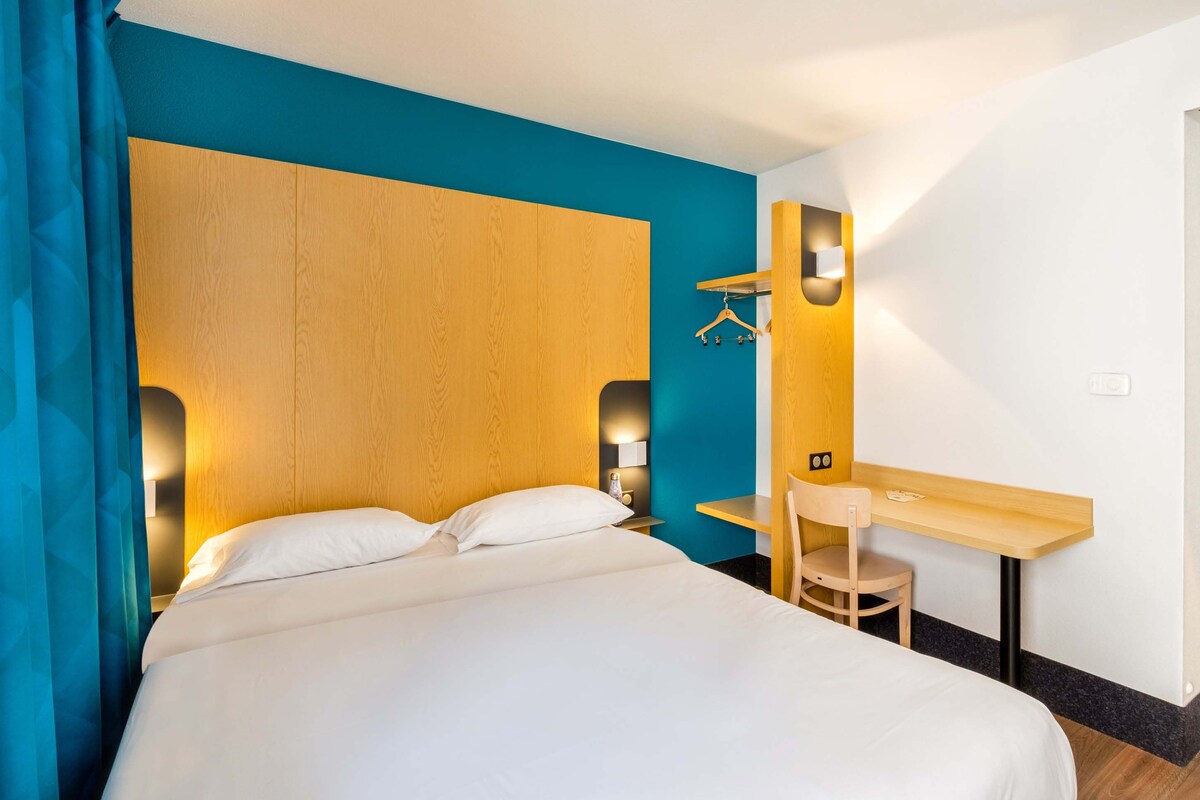A hotel room with a bed, a desk, and a chair.
