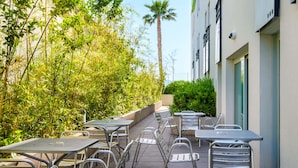 An outdoor patio with metal tables and chairs, surrounded by lush greenery and a tall palm tree. - B&B Hotel Cannes La Bocca Plage (Cannes)