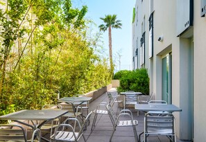 An outdoor patio with metal tables and chairs, surrounded by lush greenery and a tall palm tree. - B&B Hotel Cannes La Bocca Plage (Cannes)
