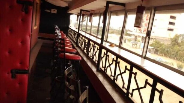 A row of red cushioned chairs with a metal railing along a balcony. - Nestwood Hotel (Nanyuki)