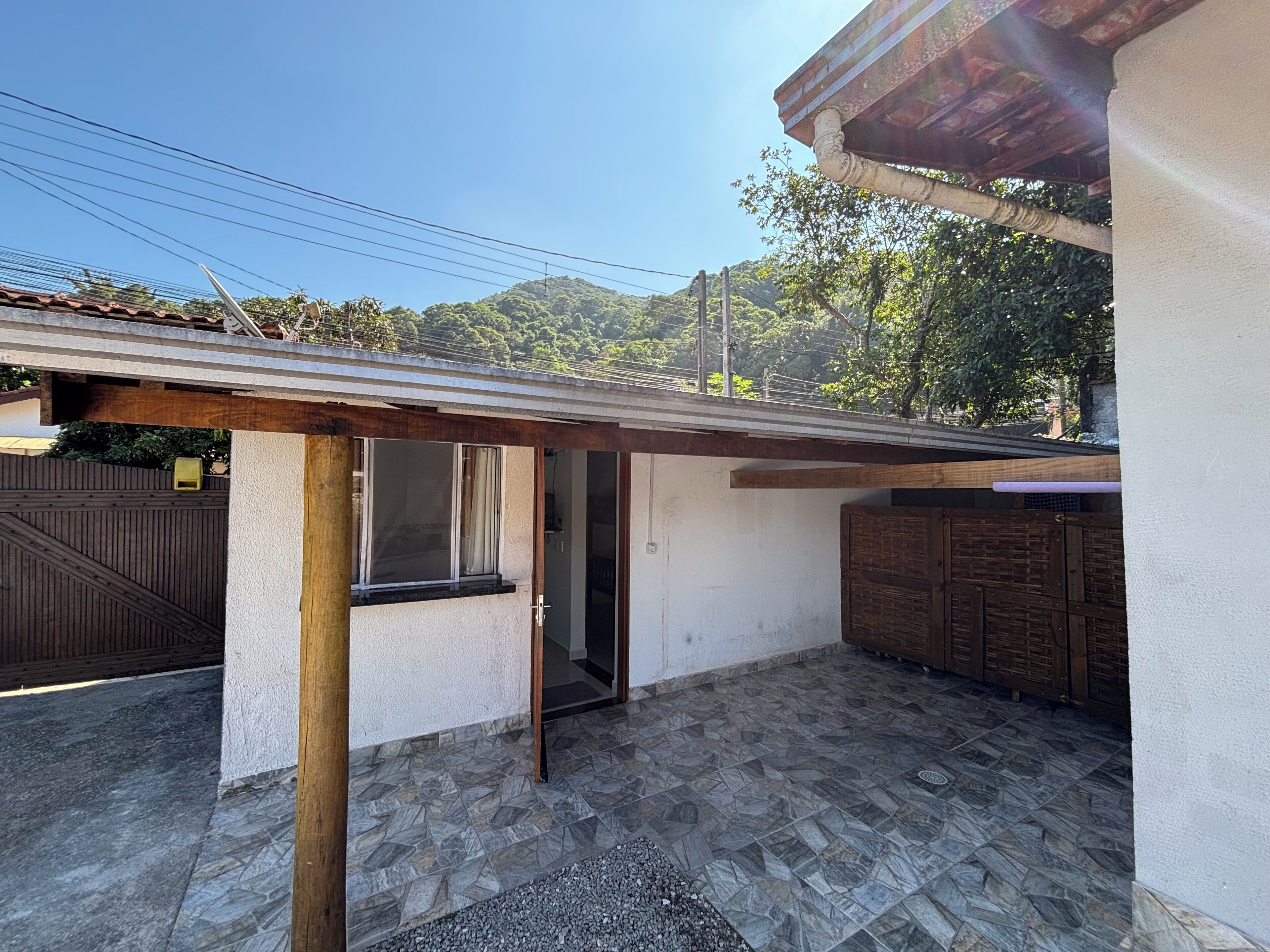 Uma área externa coberta com piso de azulejos, uma porta de madeira e uma janela.