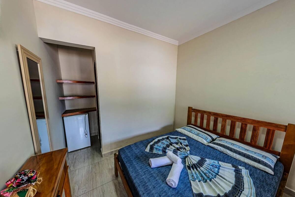 Un dormitorio con una cama, cabecera de madera, un escritorio pequeño, una silla, un armario y un mini refrigerador.