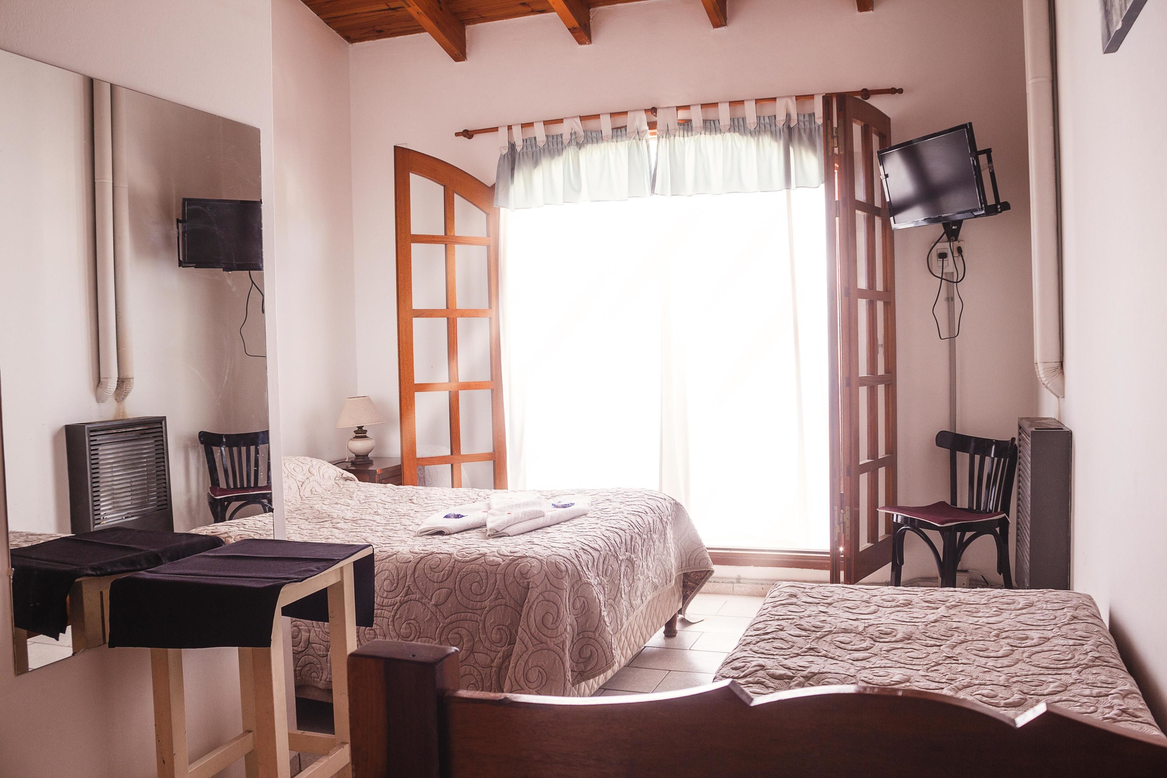 Un dormitorio con cama, escritorio, silla, televisor y ventana con cortinas.