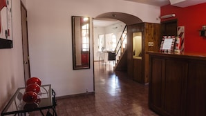 A hallway with a reception desk, a mirror, and a red wall with papers and a fire extinguisher. - Hotel Francesco (San Rafael)
