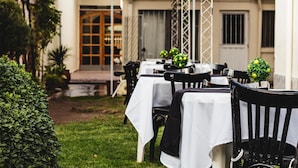 An outdoor dining area with tables and chairs, a garden, and a building in the background. - Hotel Francesco (San Rafael)