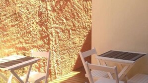 Uma área de estar coberta ao ar livre, com cadeiras e mesas de madeira branca, uma parede de areia e um deck de madeira.