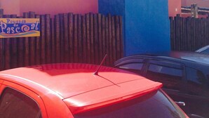 Um carro vermelho estacionado em frente a um prédio com fachada azul e rosa.