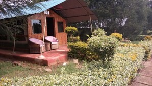 Una cabaña de madera con un porche cubierto, número 05, rodeada de un jardín con arbustos y flores variadas.