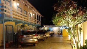 A parking area with several cars parked in front of a building with multiple balconies and a yellow wall. - Apartamentos Atobá Juquehy (São Sebastião)