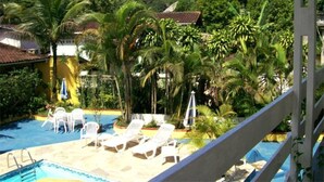 A pool area with lounge chairs and umbrellas, surrounded by lush greenery and a mountain backdrop. - Apartamentos Atobá Juquehy (São Sebastião)