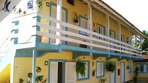 A two-story building with balconies, potted plants, and a tiled roof. - Apartamentos Atobá Juquehy (São Sebastião)