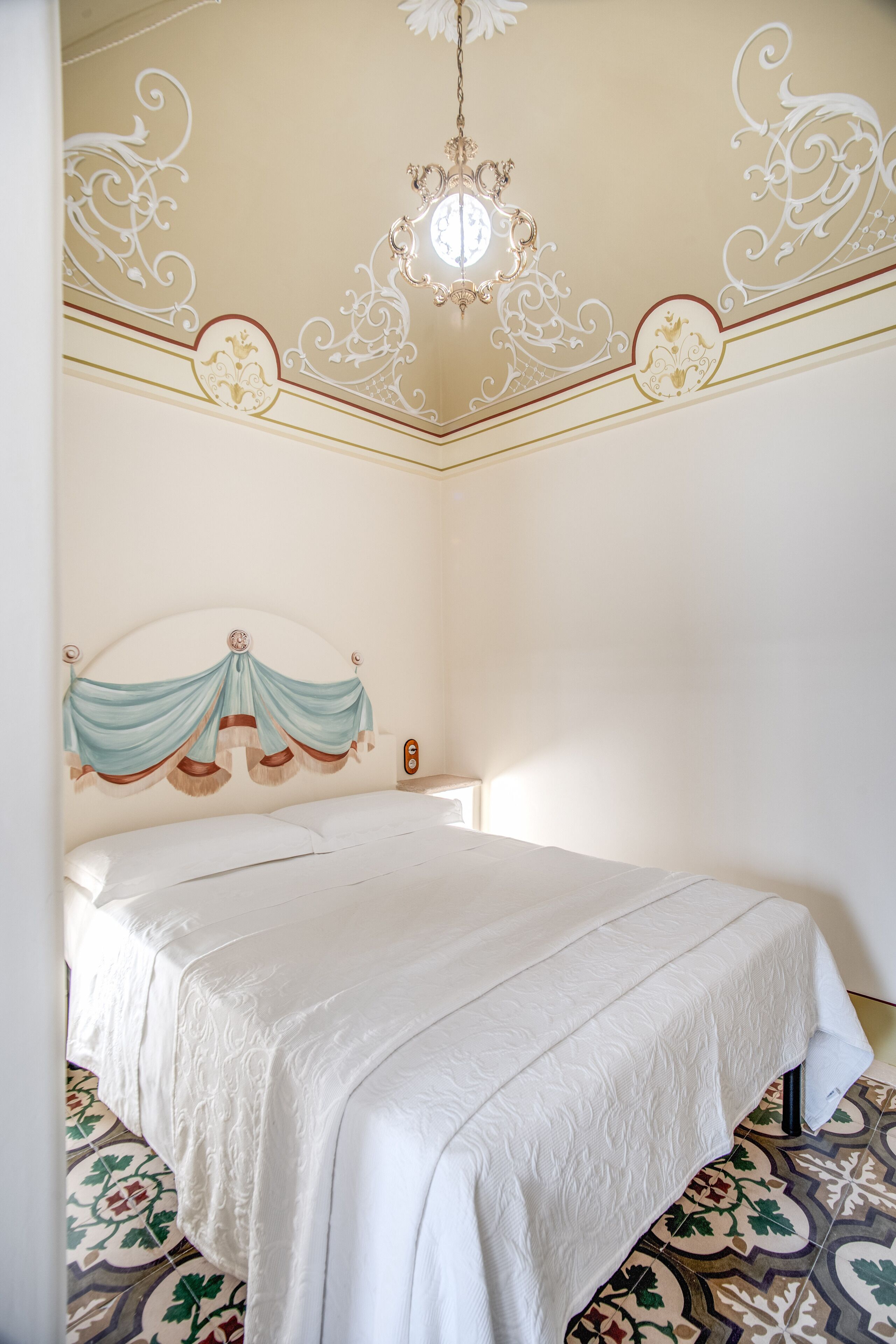 A bedroom with a bed, ornate ceiling, and patterned floor.