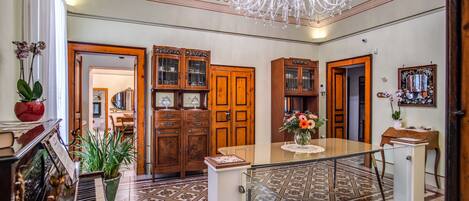 A grand foyer with a piano, wooden cabinets, a chandelier, and a patterned floor.