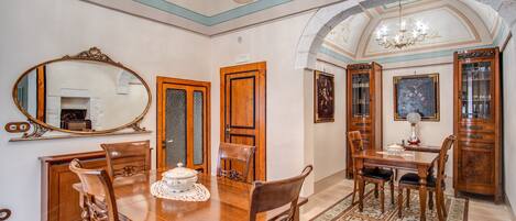 A dining room with a wooden table, chairs, a chandelier, and a large mirror.