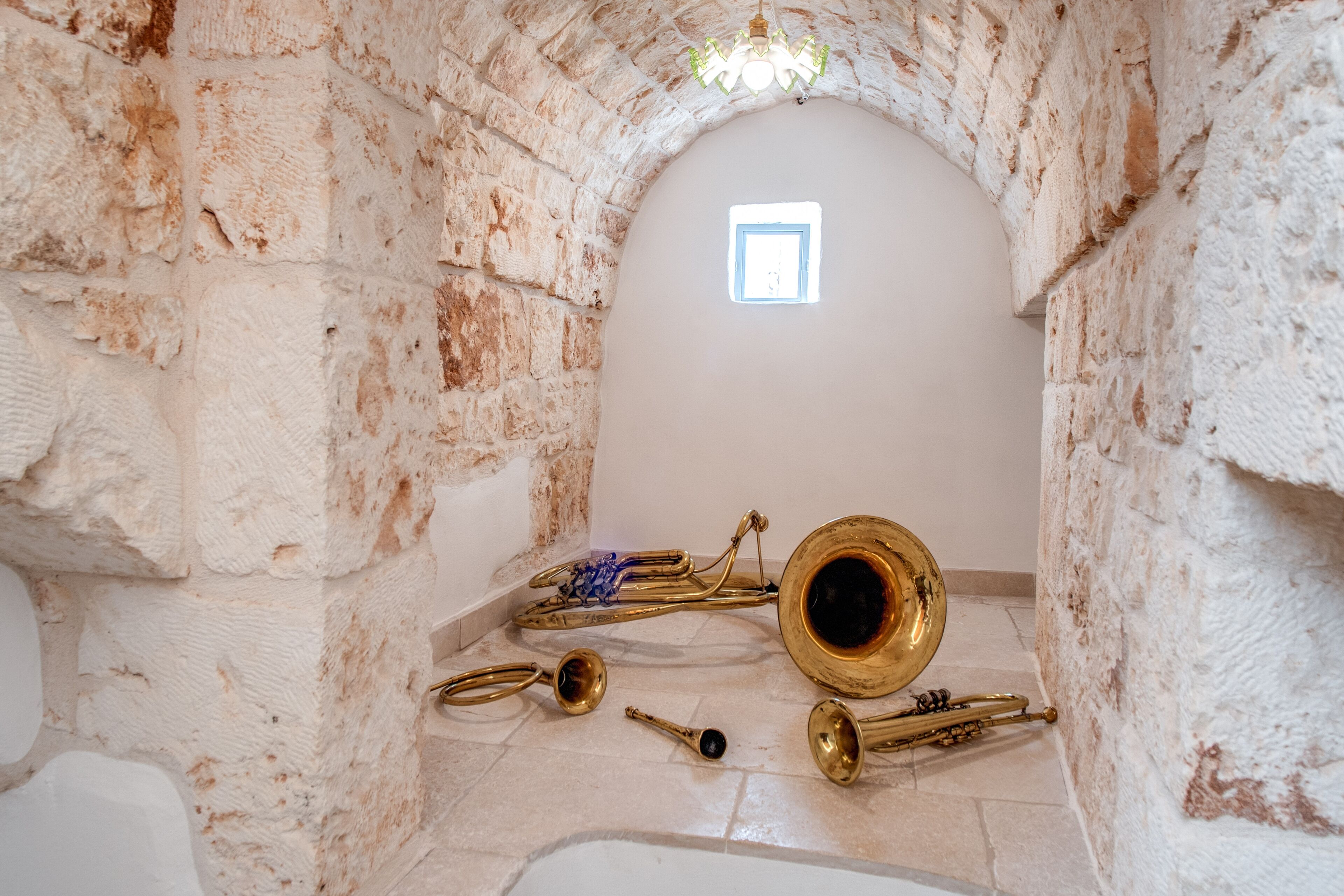 A room with a stone wall and a small window. There are brass musical instruments on the floor.