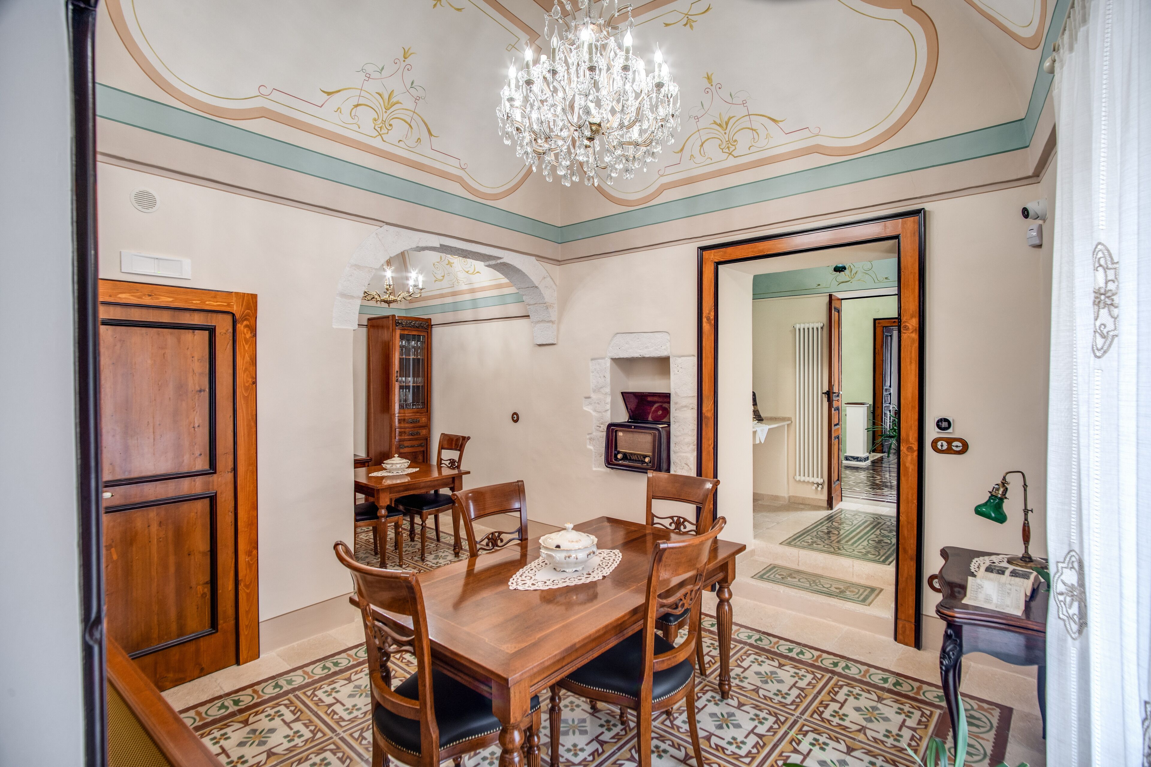 Un comedor con una mesa y sillas de madera, una araña y un suelo estampado.