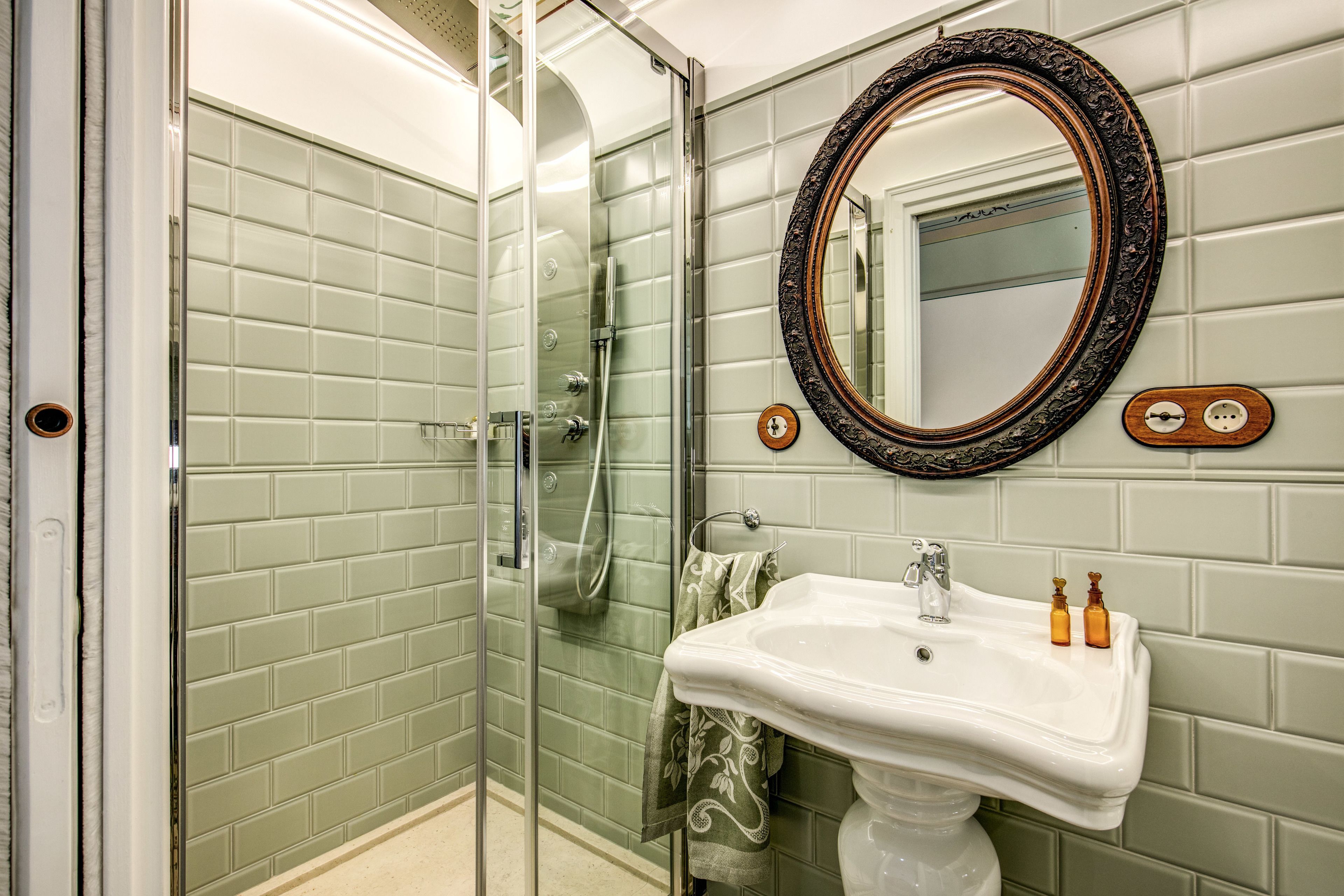 A bathroom with a glass-enclosed shower, a white sink with two soap dispensers, and a mirror with an ornate frame.
